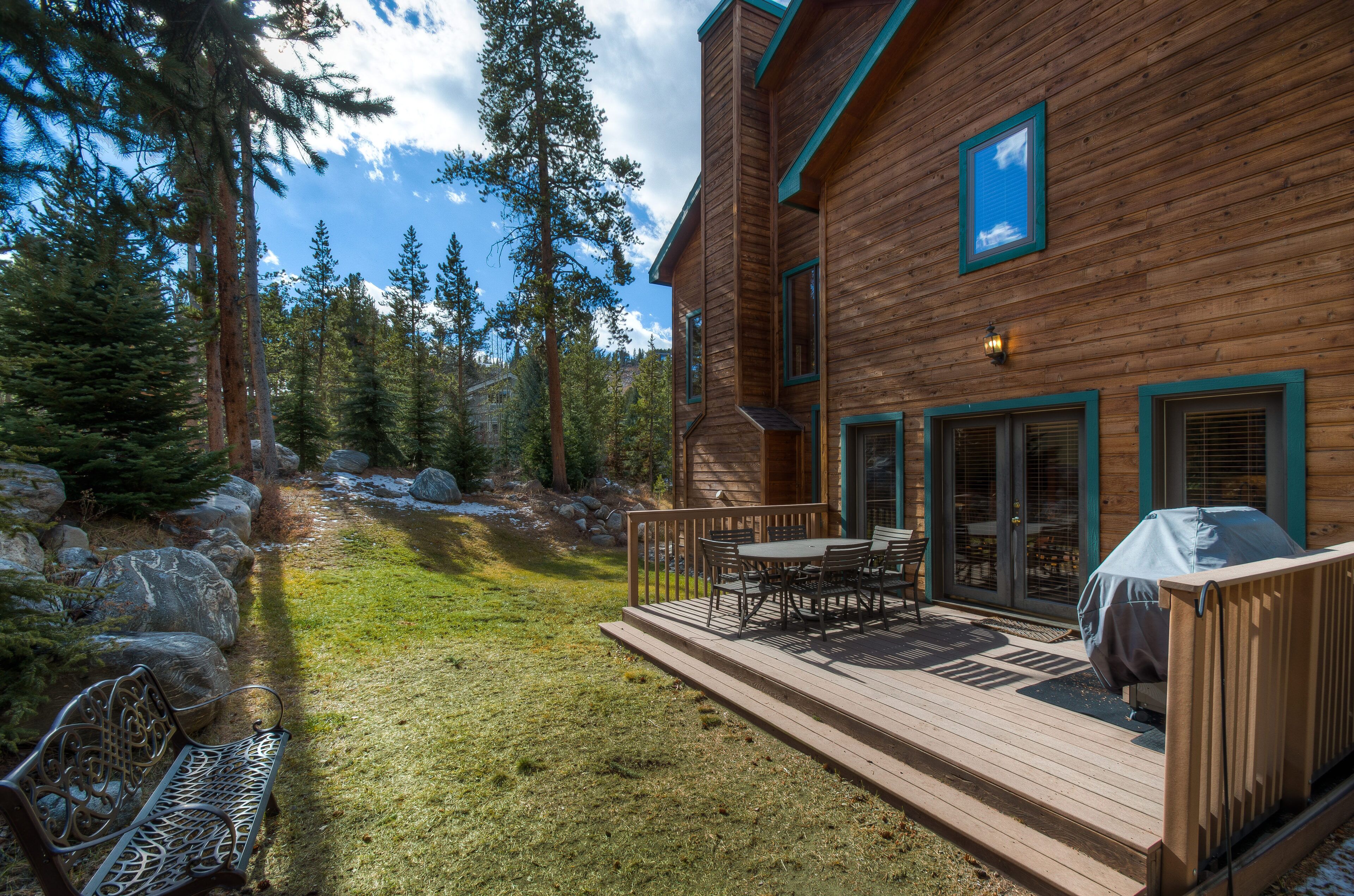 A wooden cabin with a deck, outdoor seating, and a covered grill area.
