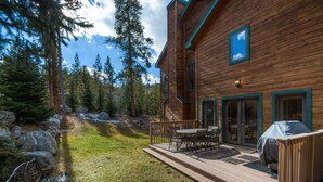 A wooden cabin with a deck, outdoor seating, and a covered grill area.