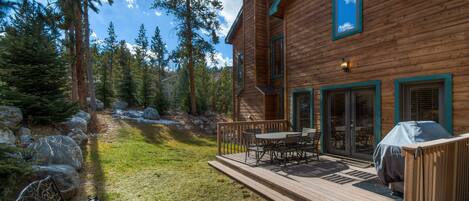 A wooden cabin with a deck, outdoor seating, and a covered grill area.