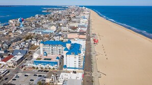 An aerial view of a coastal town with a beach, buildings, and a distinctive blue-roofed hotel.