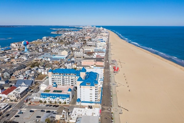 Vista aérea de uma cidade costeira com praia, edifícios e um hotel com telhado azul característico.