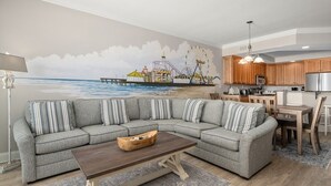 A living room with a large sectional sofa, a wooden coffee table, and a mural of a pier and ferris wheel.
