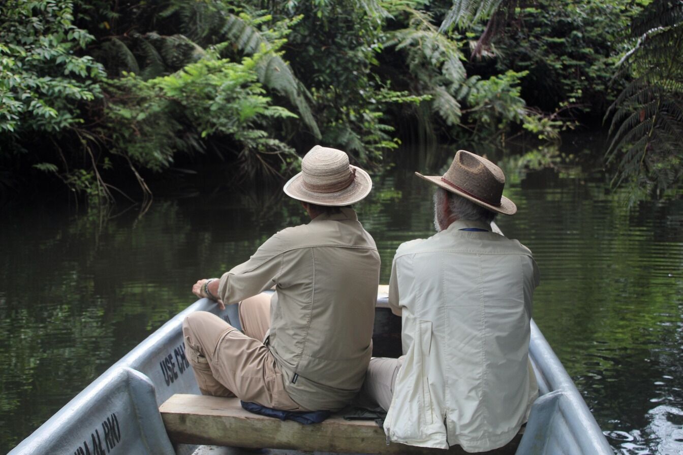 Two people in a boat on a river surrounded by dense foliage.