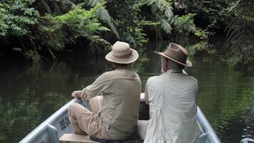 Two people in a boat on a river surrounded by dense foliage.