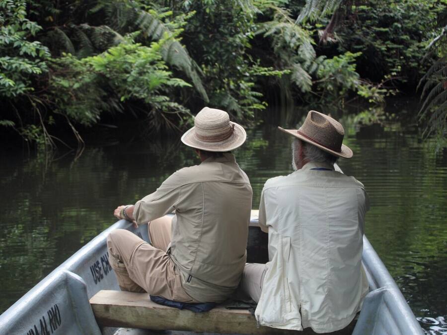 Two people in a boat on a river surrounded by dense foliage.