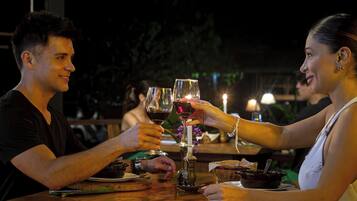 A couple toasting with wine glasses at a wooden table with a candle and a small vase.