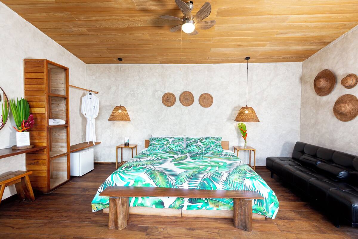 A bedroom with a bed, wooden bench, black sofa, ceiling fan, and wall decorations.