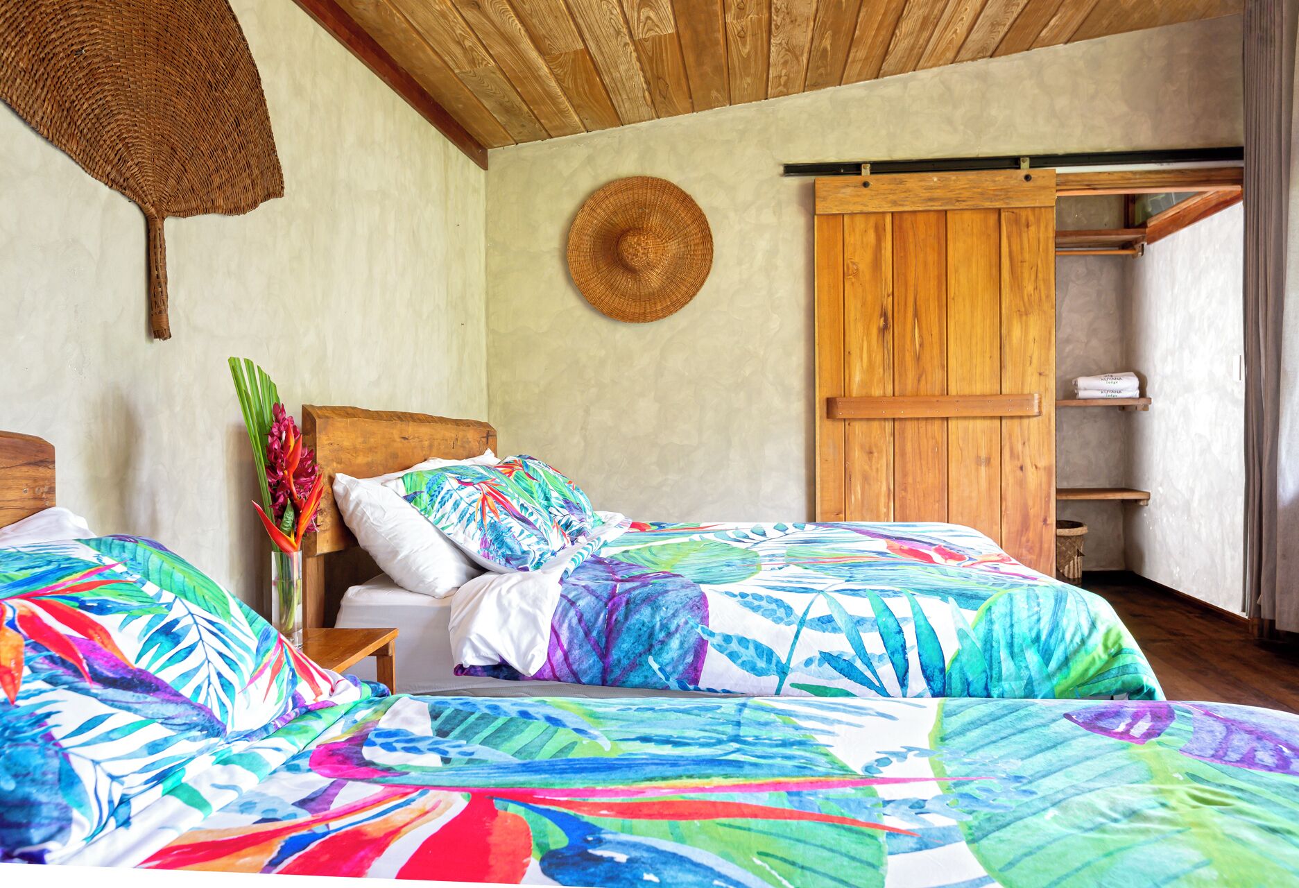 A bedroom with two beds, a wooden headboard, a woven wall hanging, and a large woven basket.