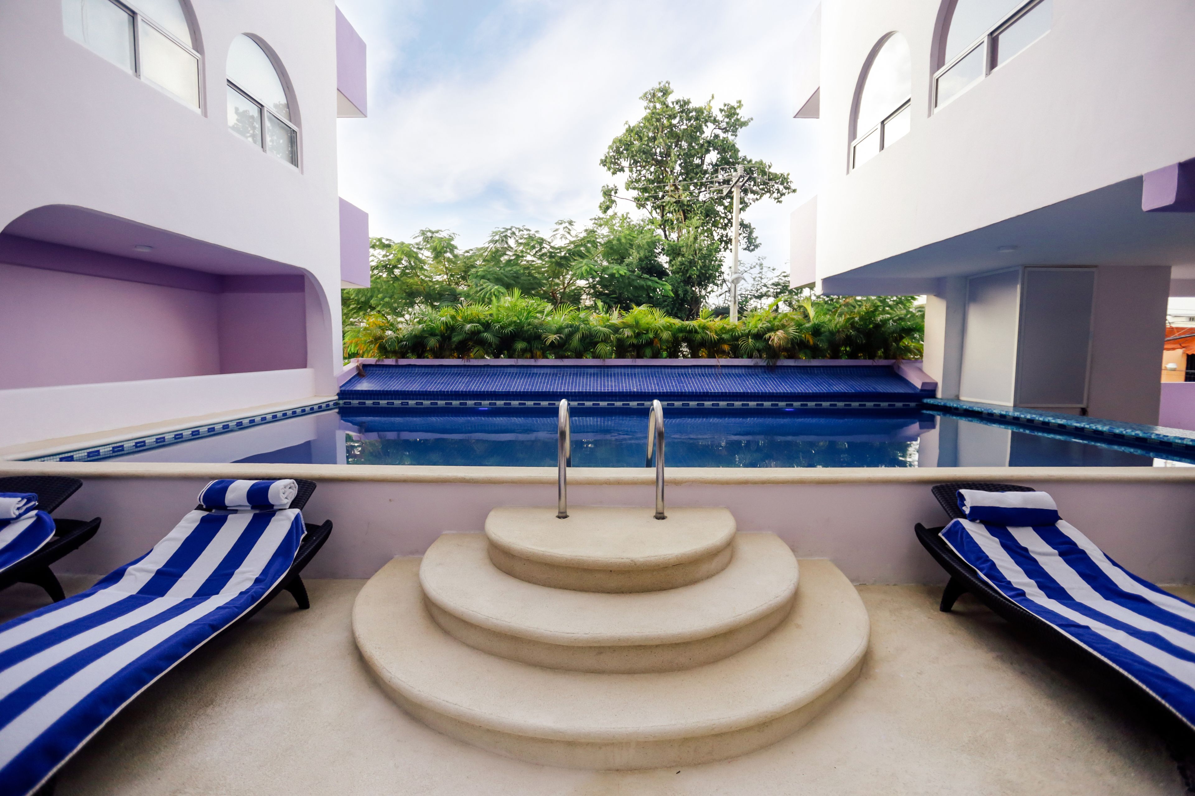 Un espace piscine avec des marches en gradin menant à l’eau, entouré de chaises longues et offrant une vue sur la verdure.