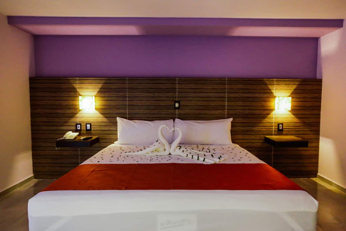 A hotel room with a large bed, two bedside tables, a wall-mounted phone, and two wall sconces.