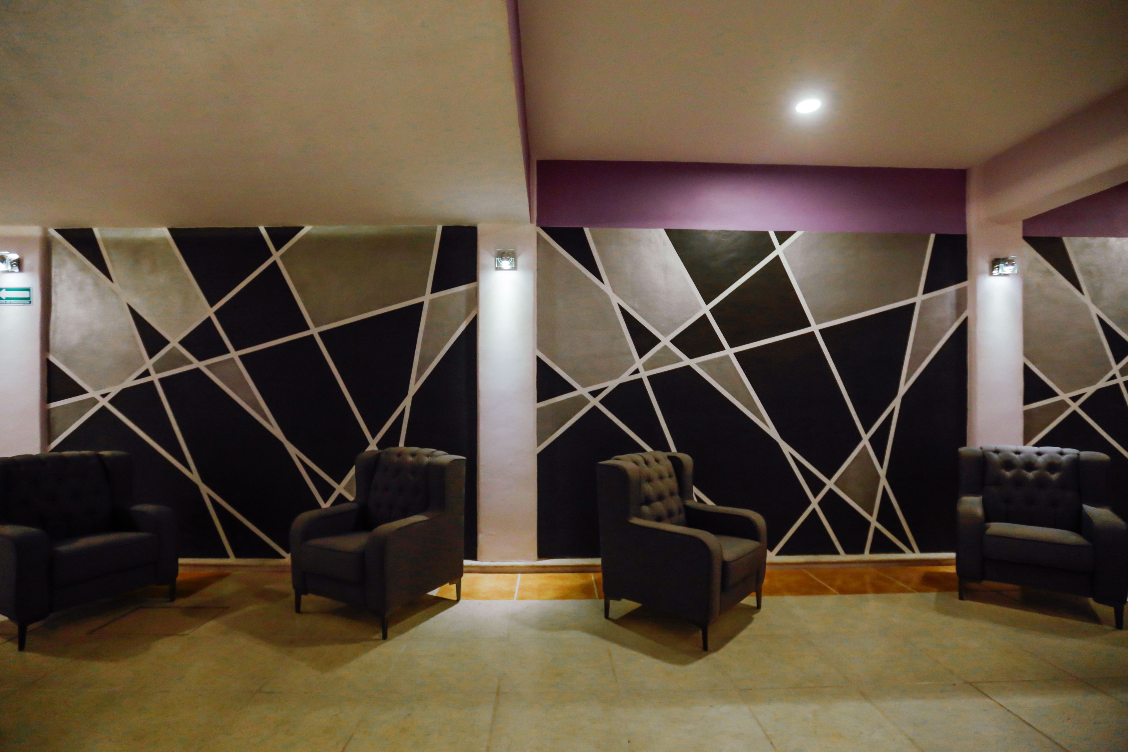 A room with a geometric wall design, three dark armchairs, and a light-colored floor.