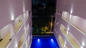 Atrio hotel di più livelli con piscina centrale, balconi e piante da interno.