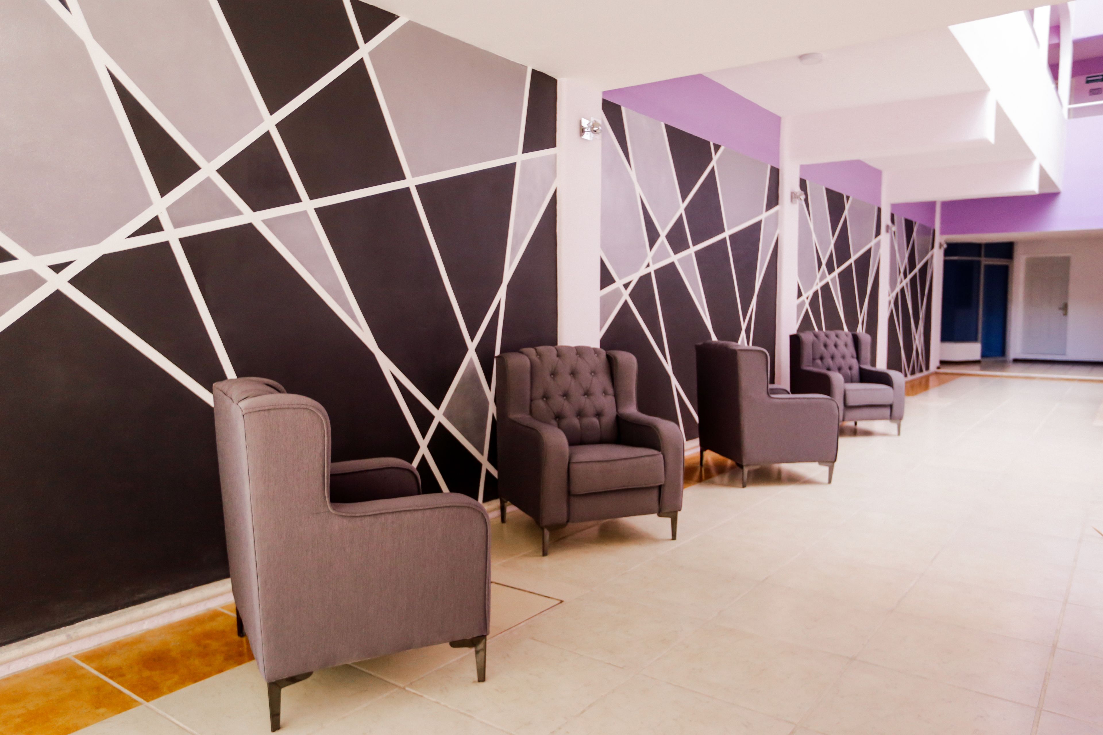 A modern hotel lobby with a row of armchairs and a geometric wall design.