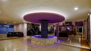 Un'ampia hall con fontana centrale, zona salotto e schermo televisivo.