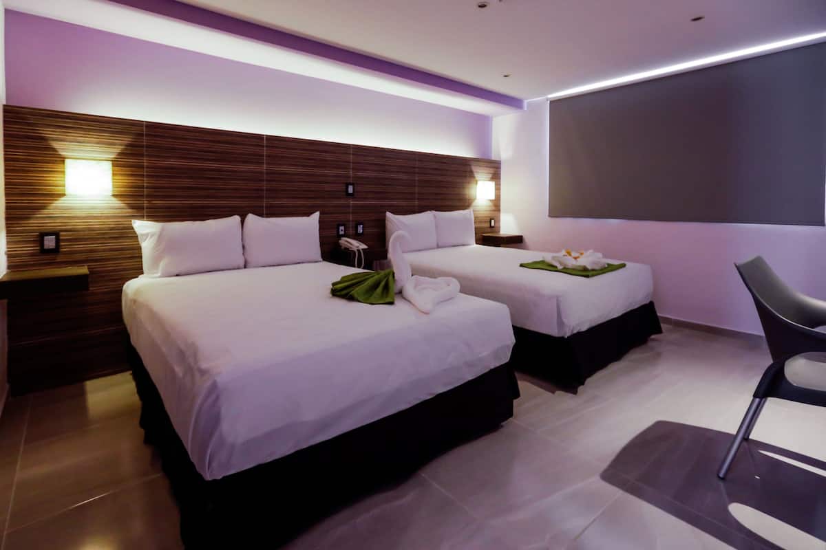 A hotel room with two beds, a flat-screen TV, a chair, and a small table with a flower arrangement.