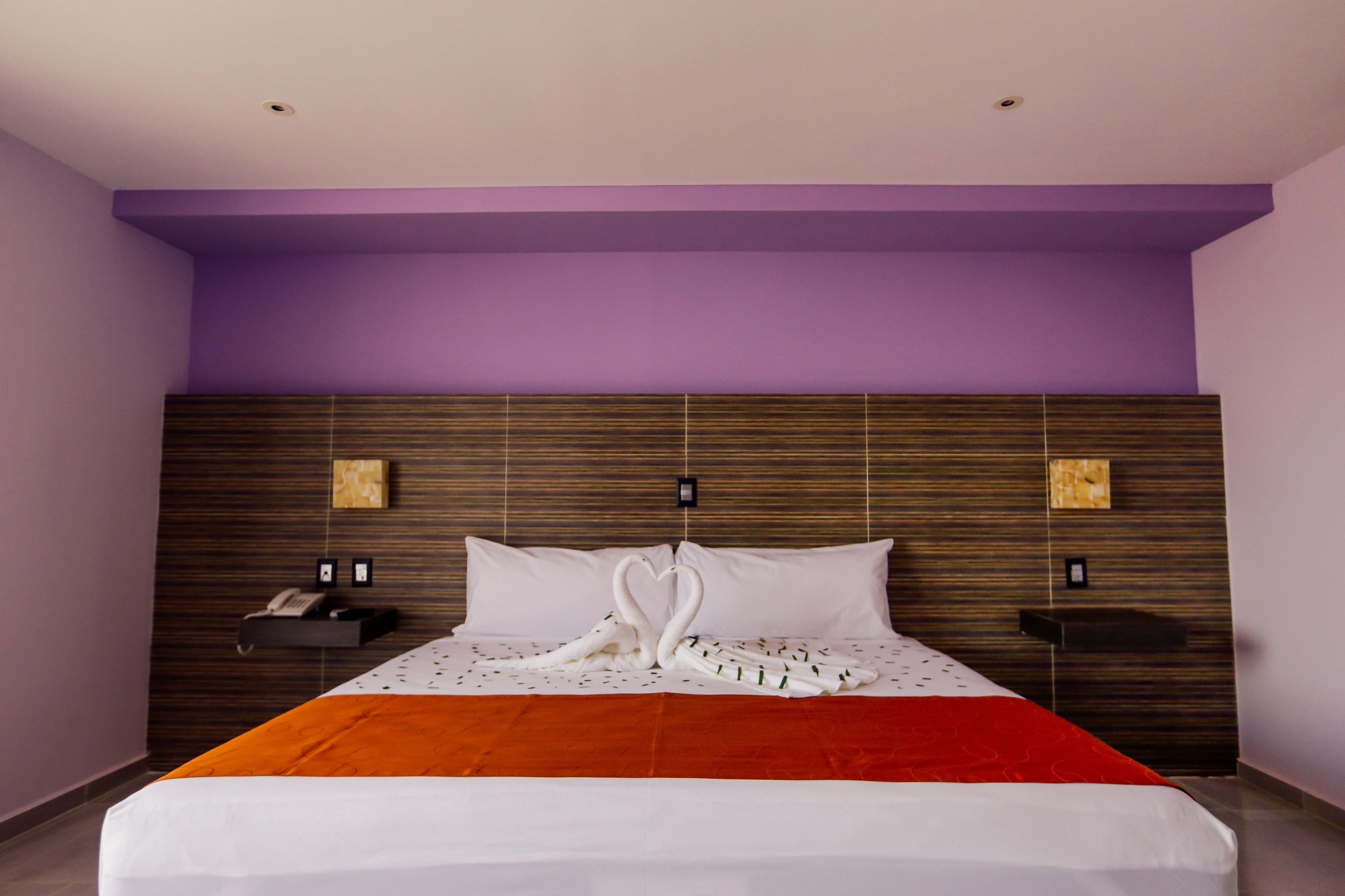 Une chambre d’hôtel avec un lit, des murs violets et une tête de lit en bois.