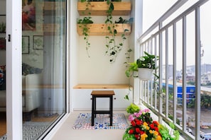 A balcony with a wooden bench, hanging plants, and a view of the city.
