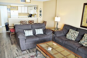 A living room with two sofas, a coffee table, and a kitchen in the background.