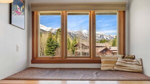Una habitación con un banco de madera, una ventana que ofrece vistas a las montañas y un cuadro en la pared.