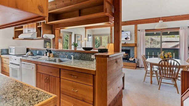 Una cocina con encimeras de granito, armarios de madera, estufa integrada y comedor con mesa y sillas.