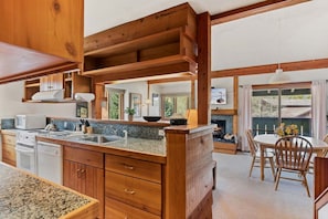 Una cocina con encimeras de granito, armarios de madera, estufa integrada y comedor con mesa y sillas.