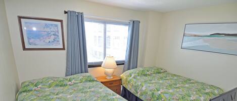 A bedroom with two beds, a nightstand with a lamp, a TV, and a window with curtains.