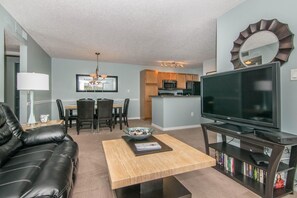 A living room with a black leather sofa, a coffee table, a flat-screen TV on a stand, and a bookshelf.