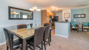 A dining area with a wooden table and chairs, a kitchen in the background, and a small seating area with a sofa and chairs. - Lake Front - 1 bedroom w/ a den 1 bath (Brandon)