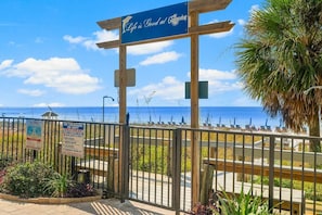 Une entrée donnant sur la plage, avec une pancarte indiquant : « La vie est belle au Commodore », un panneau indiquant la présence d’un sauveteur, et une vue sur l’océan.