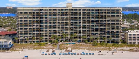 Un hotel moderno con varios balcones, una playa con tumbonas y una vista despejada del océano.