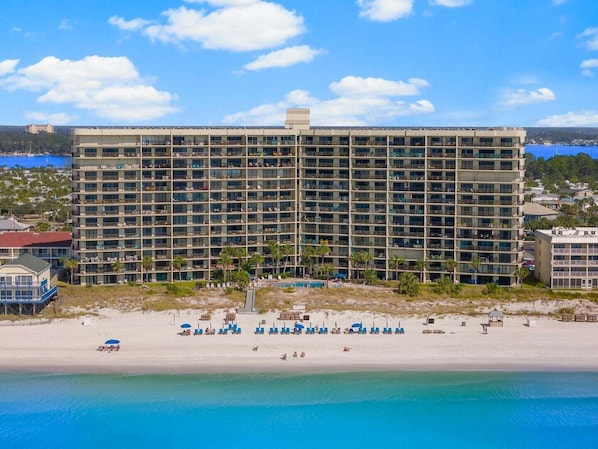 Un hôtel de grande hauteur doté de nombreux balcons, une plage avec des chaises longues et une vue dégagée sur l’océan.