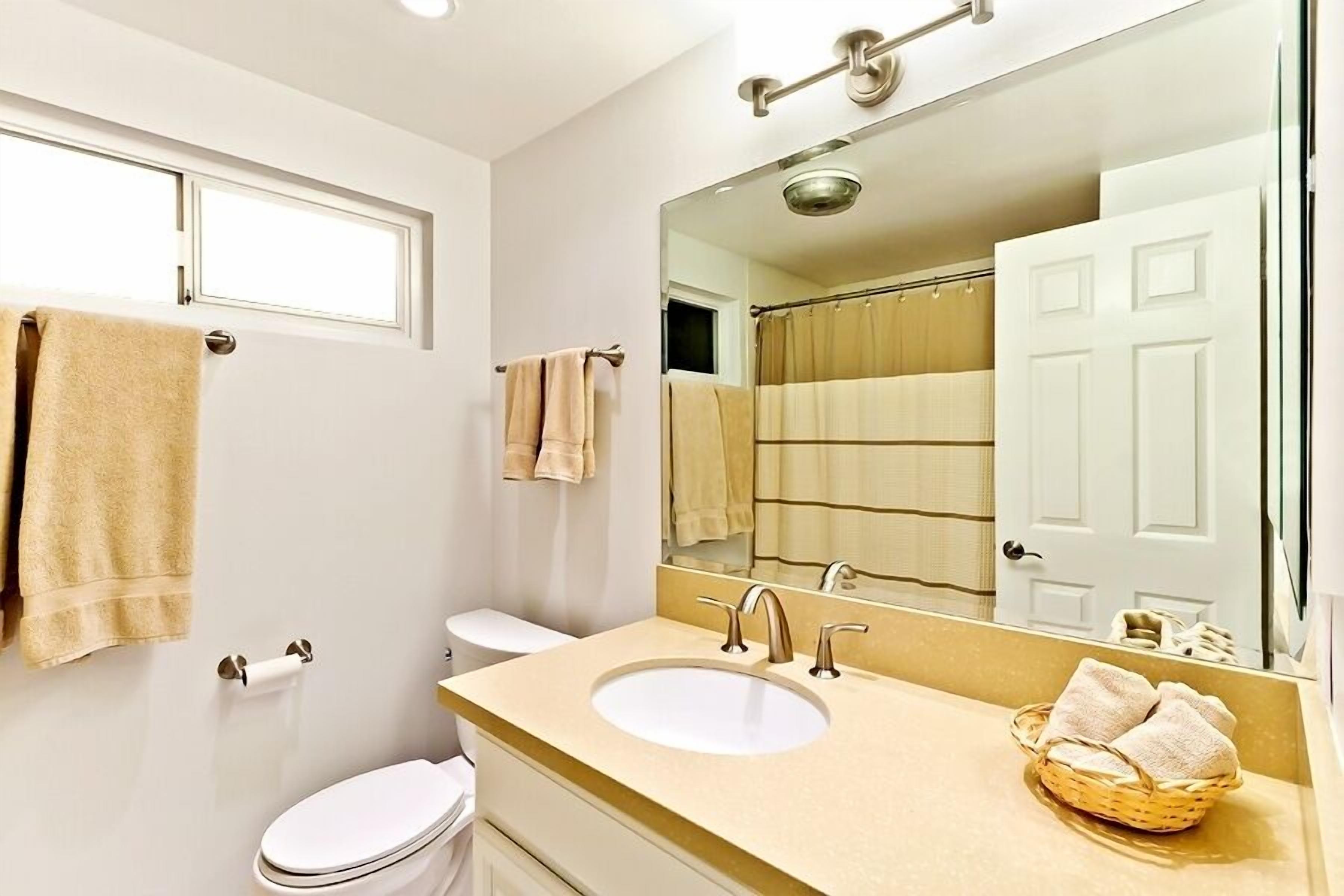 Un baño con inodoro blanco, lavamanos color beige y un espejo grande.