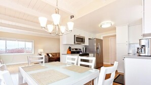 A modern kitchen with white cabinetry, a microwave, a refrigerator, and a dining area with a white table and chairs. - Beautiful Views - Sand Section of Manhattan Beach  (Manhattan Beach)