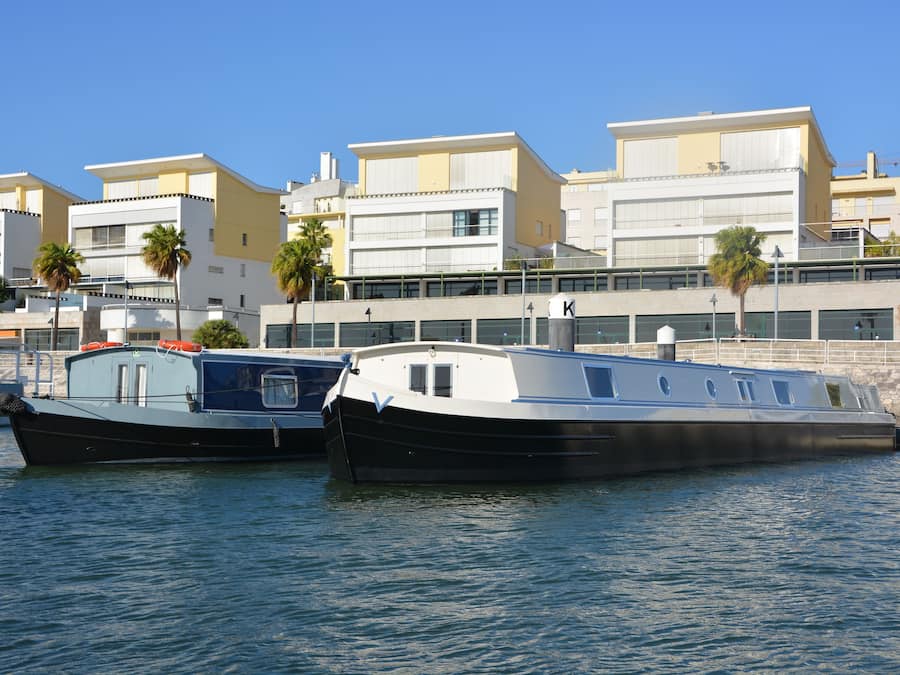 Two boats docked at a marina with buildings in the background.