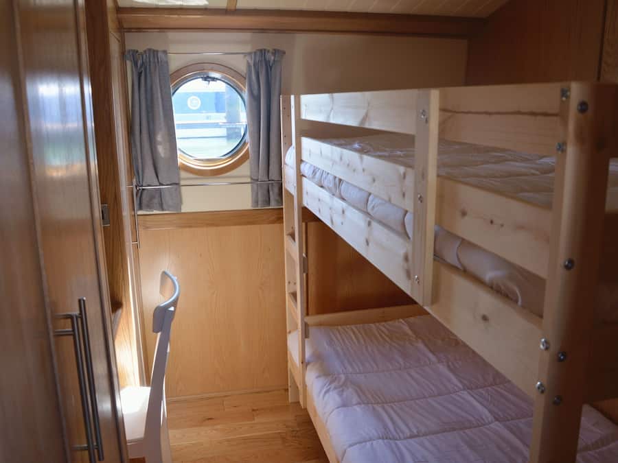 En hyggelig hytte med køjesenge, et lille vindue med gardiner og en trægulv.