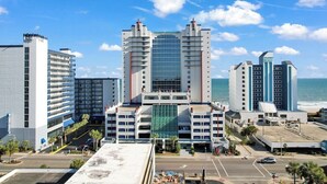 Um hotel com uma torre central de vidro, vários andares e vista para a praia.