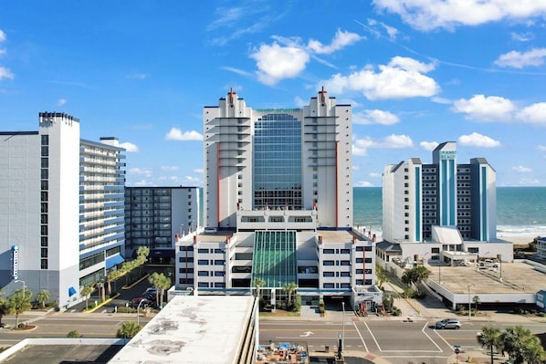 A hotel with a central glass tower, multiple floors, and a beach view.