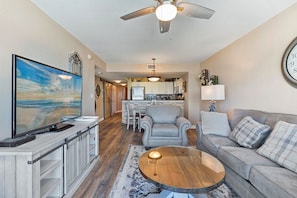 A living room with a TV, a coffee table, a sofa, and a ceiling fan.