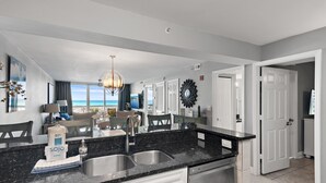 A modern kitchen with a black granite countertop, white cabinetry, and a view of the ocean through the window.