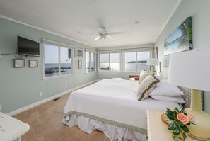 Un dormitorio con una cama grande, ventilador de techo, televisión y vista al agua.