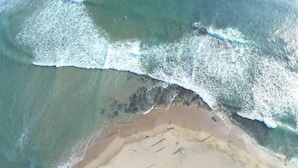 Vista aérea de una playa con olas rompiendo sobre la orilla, agua cristalina y una zona de arena.