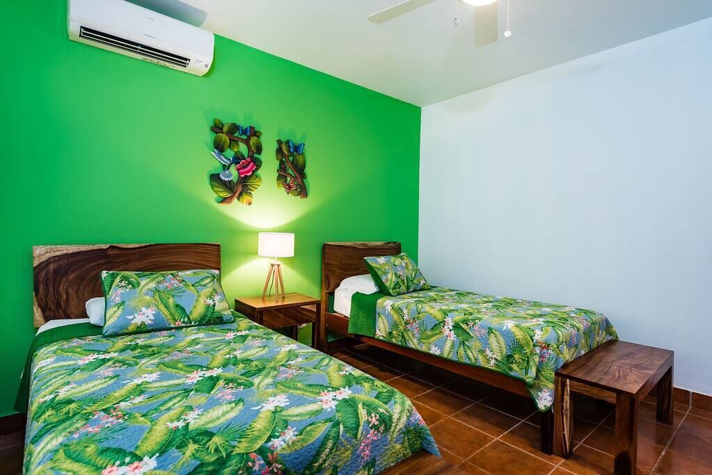 A room with two beds, a nightstand, a lamp, and a wall-mounted air conditioner.