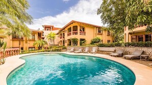 Una piscina rodeada por un edificio con balcones y un muro de piedra.