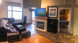 A living room with a sofa, a flat-screen TV, a fireplace, and a bed in the background.