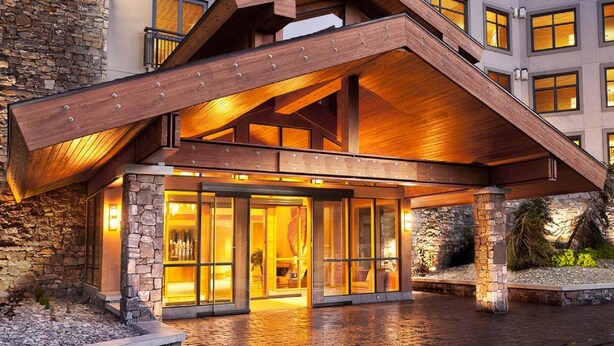A modern building with a stone facade, large glass doors, and a wooden overhang.