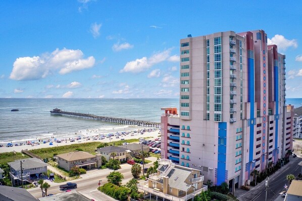 Un grand hôtel avec de nombreux étages, une vue sur la plage et une jetée en arrière-plan.