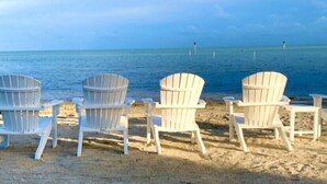 A row of white Adirondack chairs facing a beach with a calm sea and a clear sky. - Islamorada Anglers Reef! “Sandbar Bungalow Villa" AMAZING! Middle row location!  (Islamorada)