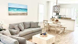 A spacious living room with a large gray sofa, a striped armchair, and a wooden coffee table. A painting of a beach is on the wall, and a ceiling fan is visible. - Islamorada Anglers Reef! “Sandbar Bungalow Villa" AMAZING! Middle row location!  (Islamorada)