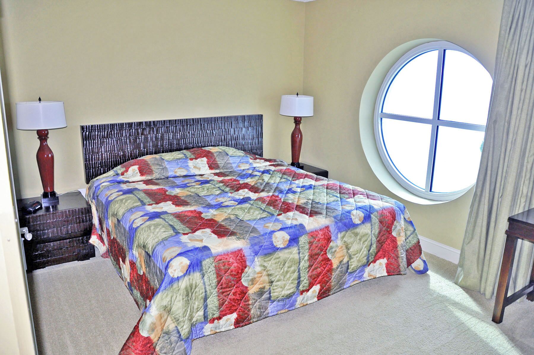 A bedroom with a bed, two bedside lamps, a round window, and a headboard.