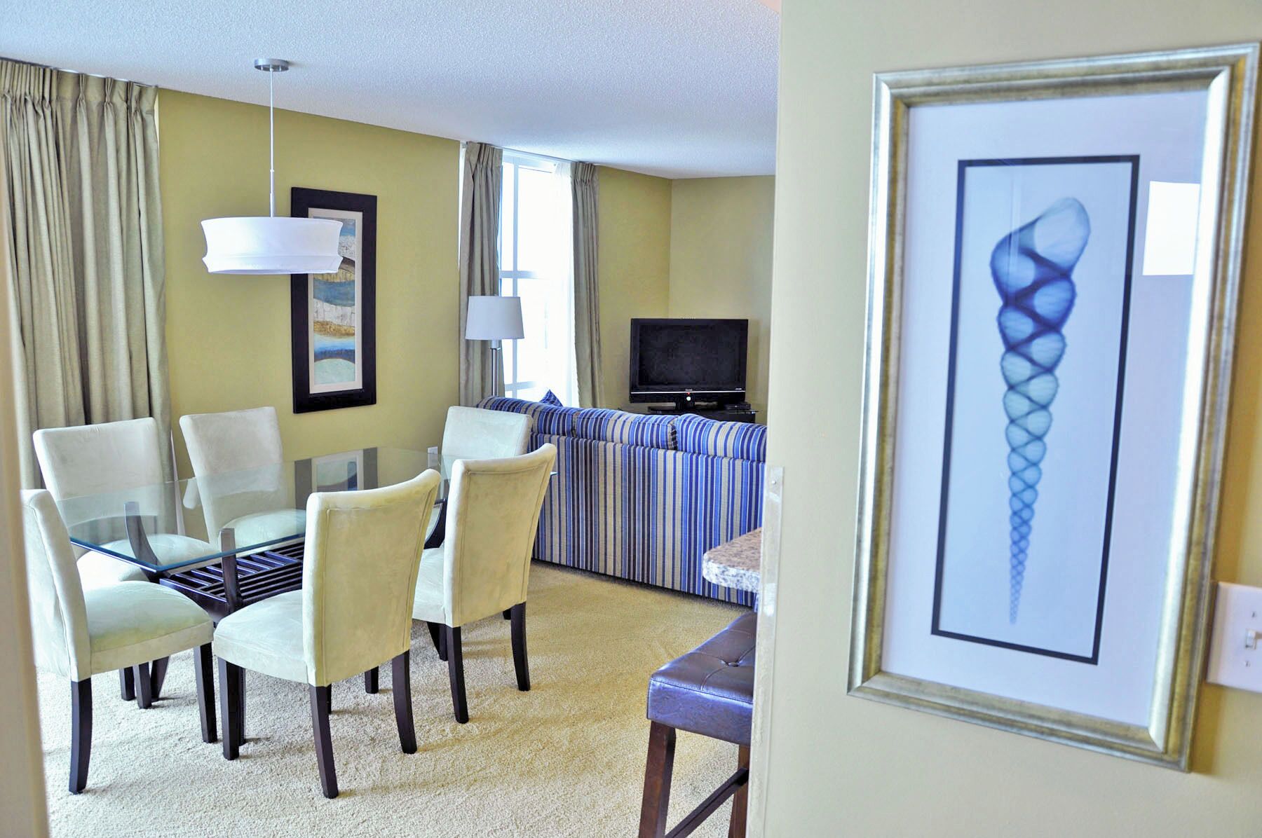 Habitación de hotel con una mesa de comedor, sillas, un sofá, un televisor y un cuadro en la pared.